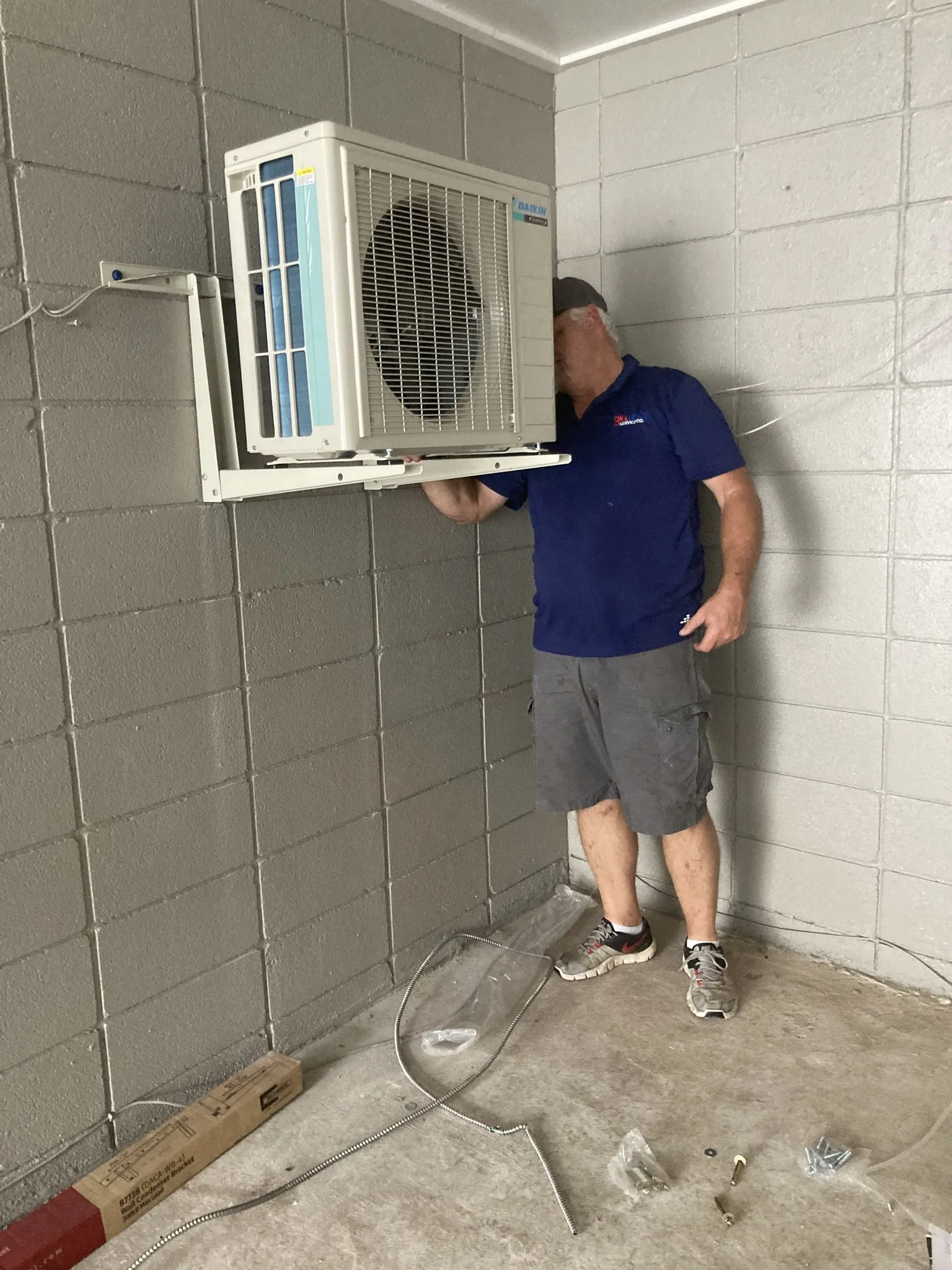 Technician installing a Daikin outdoor air conditioning unit on a concrete wall